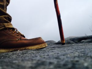 An up close shot of a hiker with a cool walking stick making the venture out onto some high rocks.